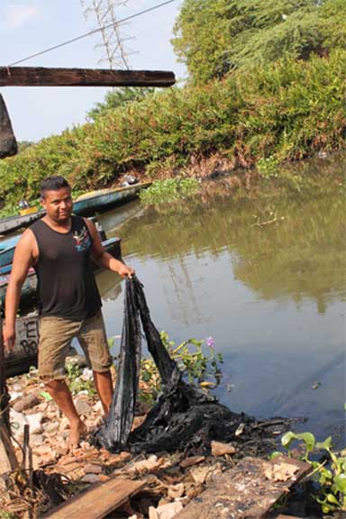 A fisherman in a rural village nearby Lagunillas on the east cost of Lake Maracaibo shows an oil stained net, turned black after a single day of use. Photo by María Carlota Marval