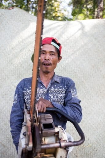 A villager from Mahu poses with his chainsaw in front of one other source of meager local income: a mat made of dry bamboo. Photo by Ann Wang for Mongabay.