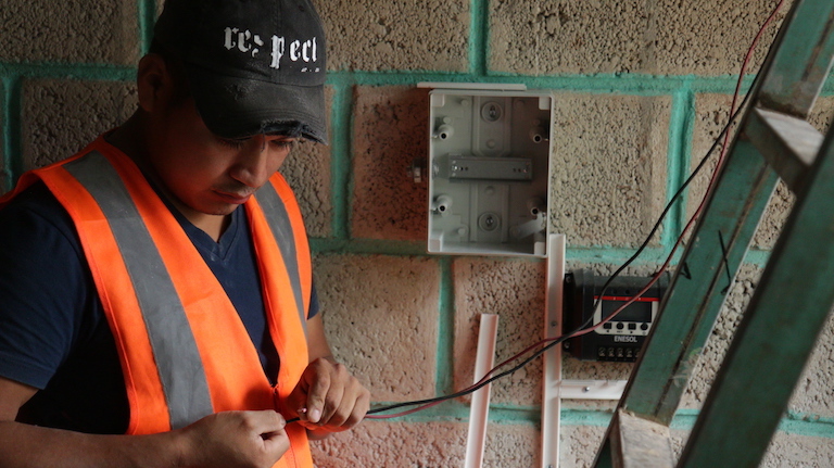 Miguel Angel, one of the Tosepan cooperative’s team of young solar panel installers, hooks up deep-cycle batteries and a fuse box at Doña Mari’s house. Image by Ethan Bien for Mongabay.