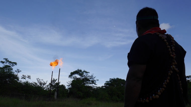 Emergildo Criollo looks on at a gas flare near an oil refinery some 20 miles from Lago Agrio, at dusk. The flares, a common sight in the region, burn off gas from piped oil. Image by Dan Collyns for Mongabay.