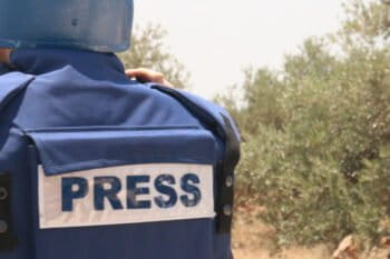 A journalist in a borrowed flak jacket and helmet works in Ni'lin, West Bank in June 2016. Photo by Genevieve Belmaker/Mongabay.