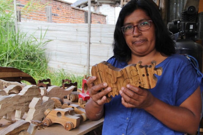 Susana Simbana holds a 3D puzzle of a cow, which she designed and made, while standing in front of more of her creations. Photo by Kimberley Brown for Mongabay.