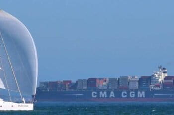A modern sailing vessel passes a fossil-fueled container ship. Image via Visualhunt.
