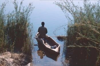 Lone figure in dugout canoe emerging from reeds on river. Image by Patrik M. Loeff via Flickr (CC BY-NC-ND 2.0)
