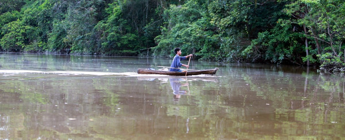 A member of the Indigenous Tikuna nation paddling a dugout canoe on a tributary of the Amazon in Colombia by Rhett A. Butler/Mongabay.