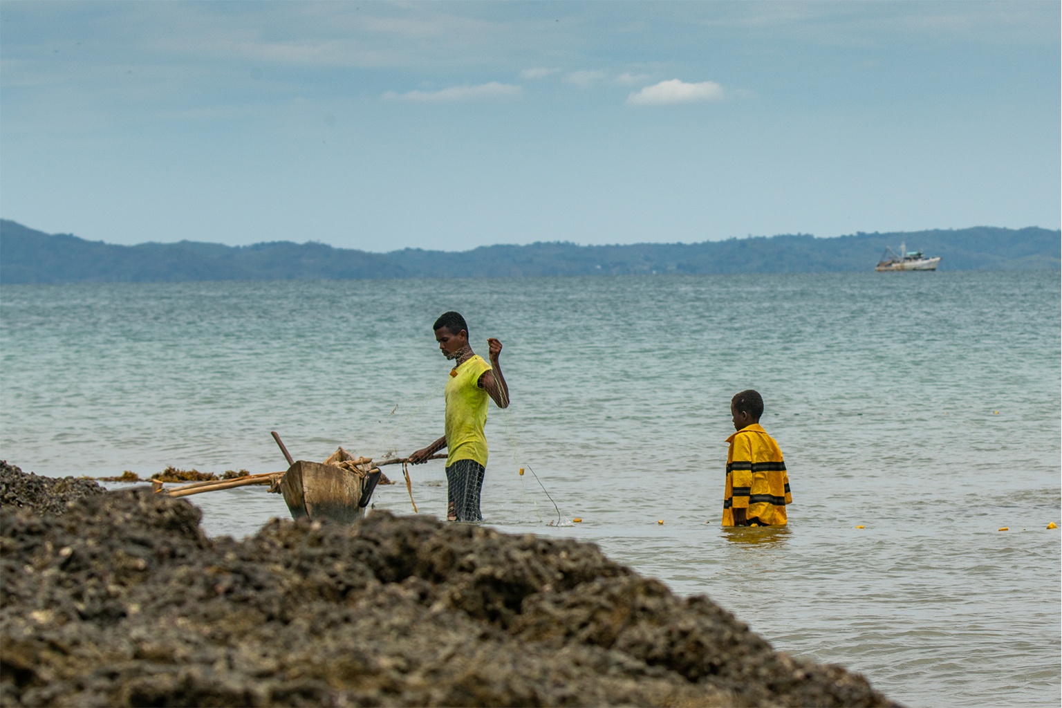 Small-scale fishers set a net close to shore on Nosy Faly as an industrial trawler fishes further offshore.