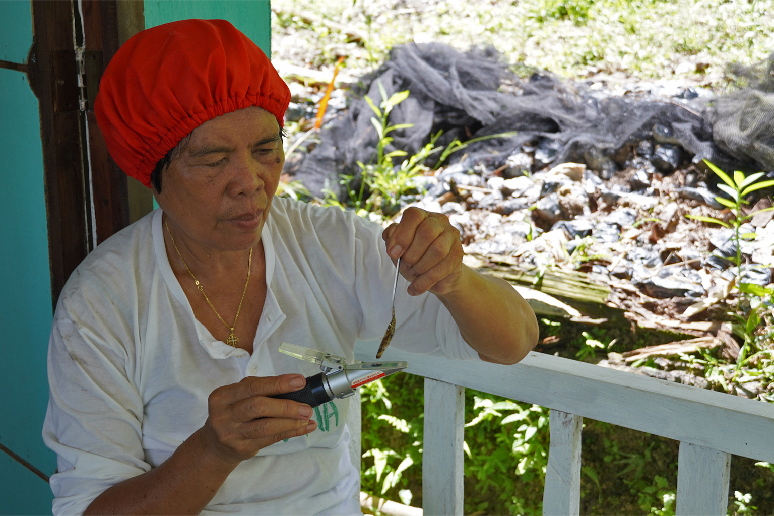 Macatumbalen village leader Nida Collado sits at the government-funded honey processing house as she measures honey moisture content with a refractometer to ensure it meets market quality standards.