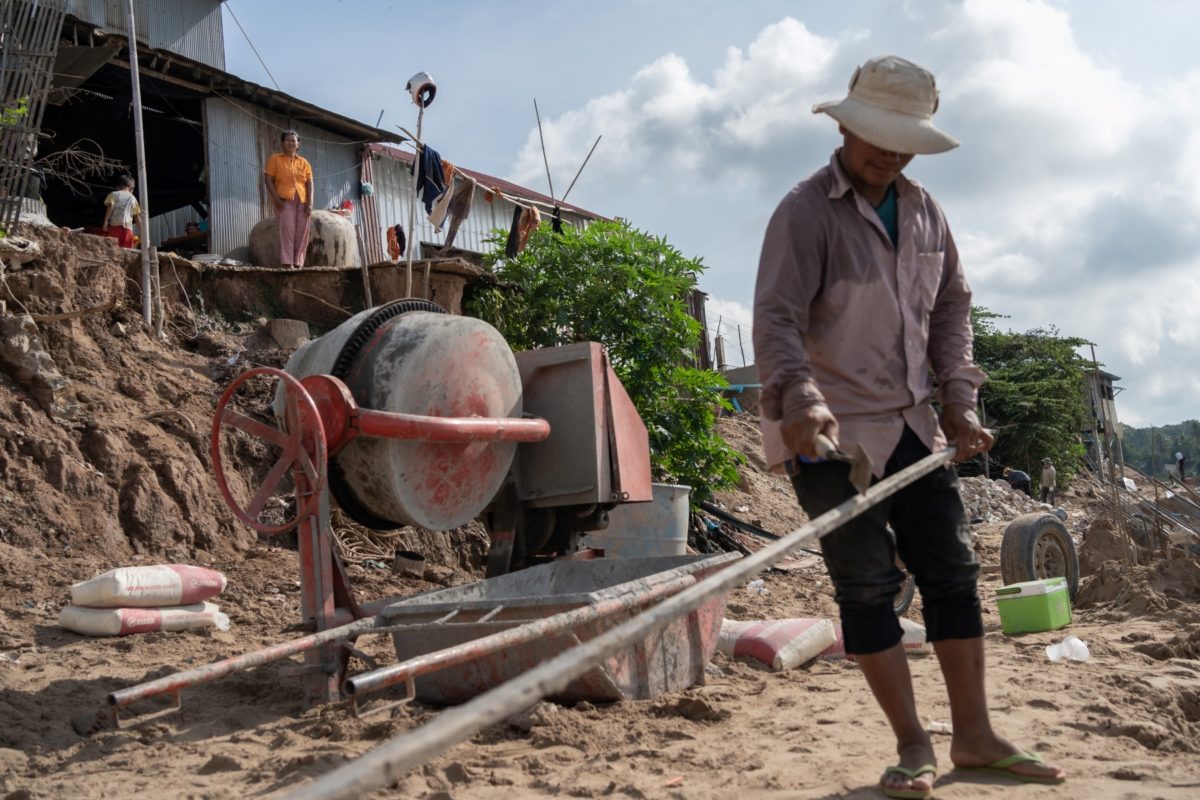 Workers repair the riverbank as a resident watches on from her house.