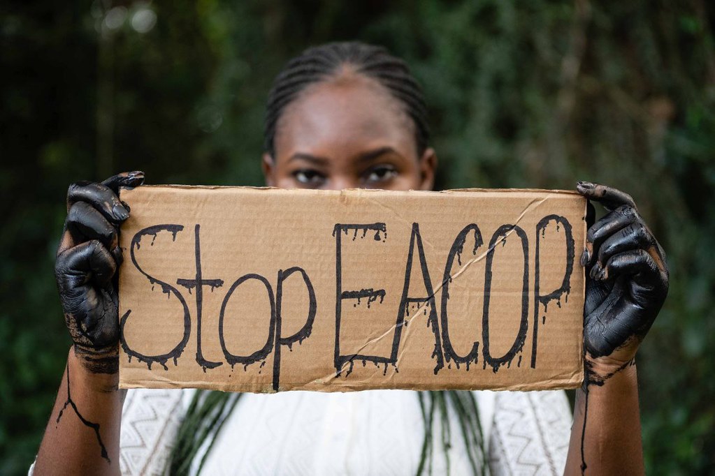 Person holding cardboard sign saying Stop EACOP", concealing lower half of their face. Photothèque AT via Flickr (CC BY-NC 2.0)