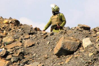 Tanzanian police officer in dull green riot gear and helmet, pictured against the sky guarding waste dump site at Barrick Gold's North Mara mine. Image courtesy Catherine Coumans / Mining Watch.