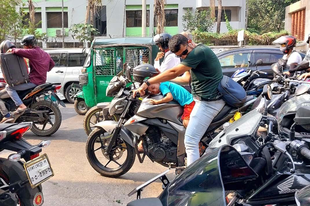 A child falls asleep on the motorbike tanker as the man riding the bike in Dhaka looks exhausted 