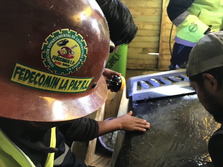 Miners at Águilas de Oro huddle over the gravitation table, shining a torch to see the specks of gold. Image by Thomas Graham for Mongabay.