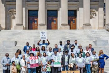 Greater Greener Gloster community members stand in front of the state capitol in Jackson, Mississippi, as they demand the cleanup of the Drax pellet mill