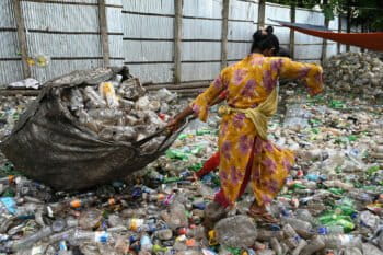 A woman pulls a large bag filled with plastic in a landfill in Bangladesh.