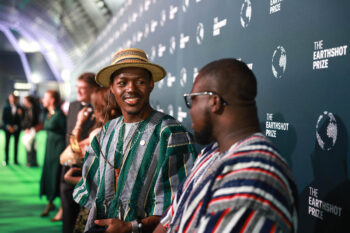 Tastefully-hatted Desmond Alugnoa smiles at project manager Jakob Attakpah in front of an Earthshot Prize banner. Image courtesy Earthshot Prize.