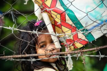 A little girl looks out between the barbwire of the refugee compound in 2015.