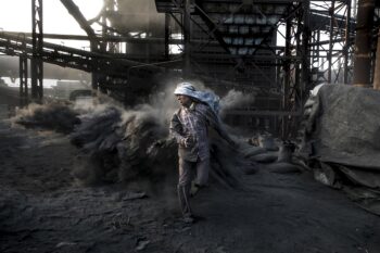 A coal miner walking barefoot through heaps of coal dust at a coal mine and processing plant, Jharkand, India. Image courtesy of Rajesh Kumar Singh / Climate Visuals Countdown.