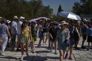 Tourist with umbrellas wait outside the Acropolis of Athens, on Monday , July 7, 2025 while authorities in Greece have imposed mandatory work stoppages in parts of the country where temperatures are expected to exceed 40 degrees Celsius (104 Fahrenheit) (AP Photo/Petros Giannakouris)