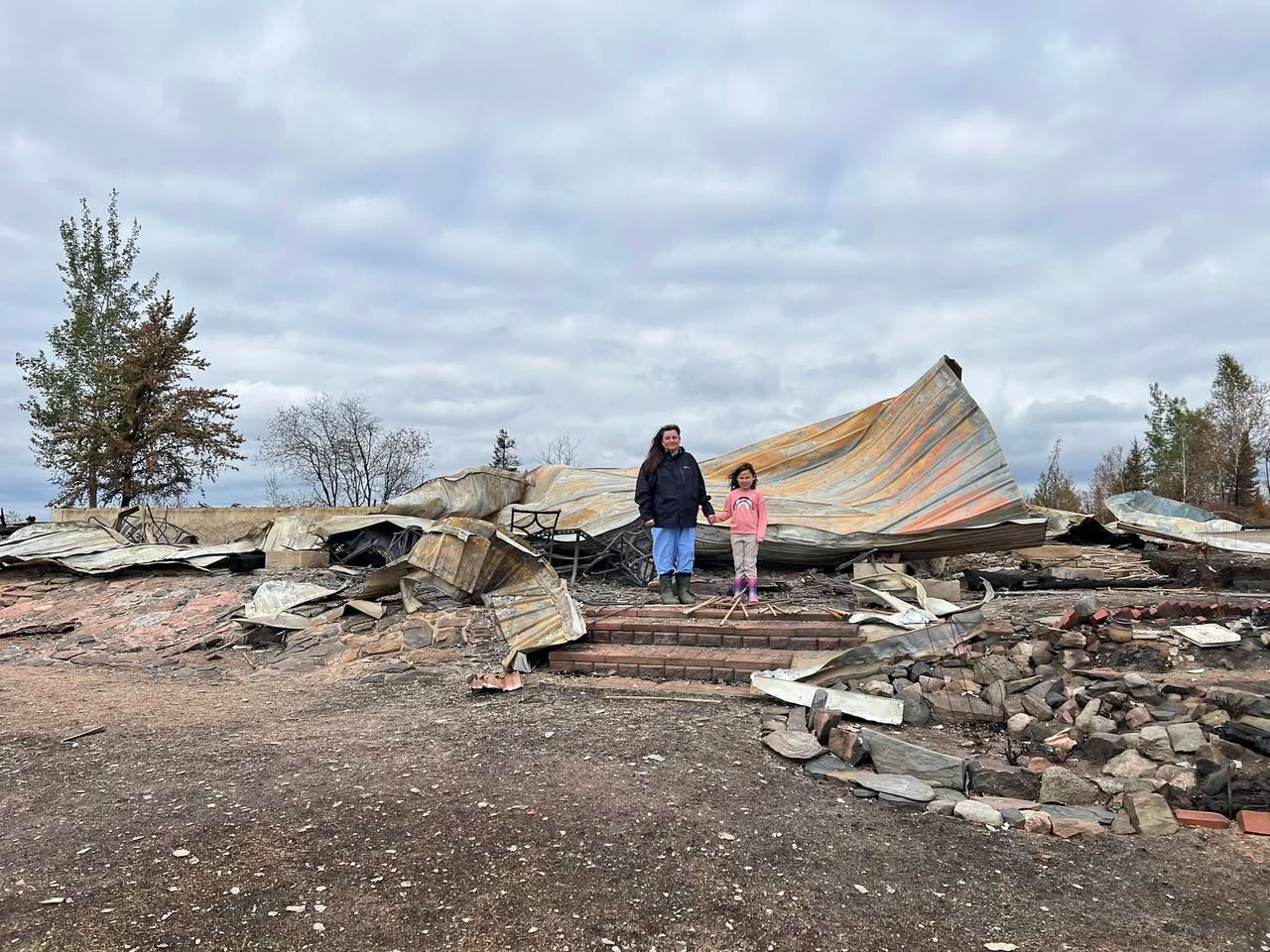 A young girl and her grandmother stand on the shore of a northern Saskatchewan lake, where a wildfire recently claimed the family cabin