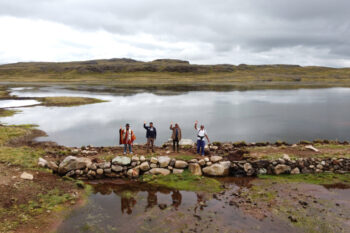 4 people standing in front of a lake waving.