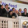 JBS founder José Batista Sobrinho (center) flanked by his sons, Joesley (taking a selfie) and Wesley (clapping), waves from the podium after ringing the New York Stock Exchange opening bell, Wednesday, June 25, 2025. Image by AP Photo/Richard Drew.