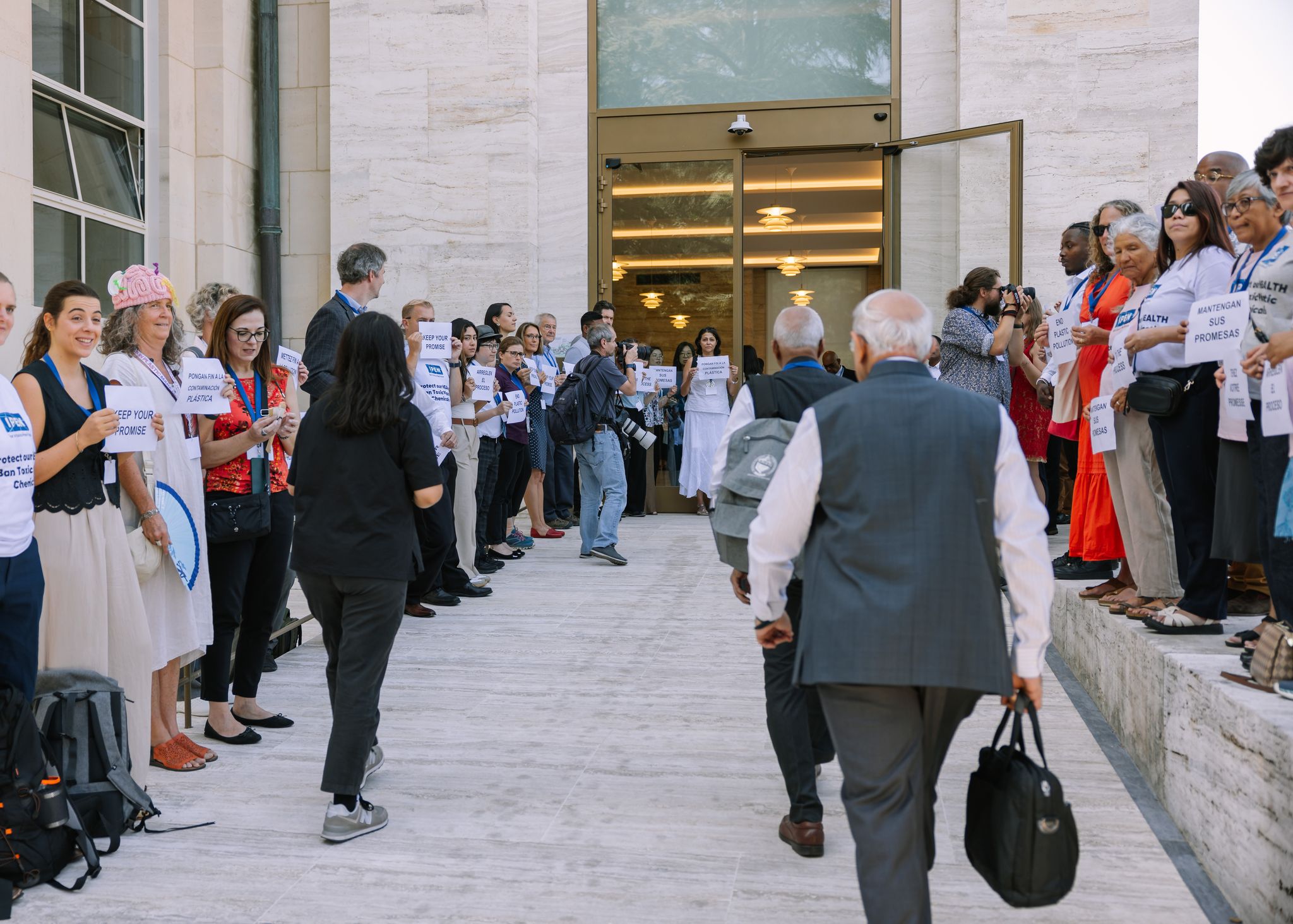 Peaceful protestors look on as plastics treaty negotiators walk past on their way into the INC-5.2 summit in Geneva.