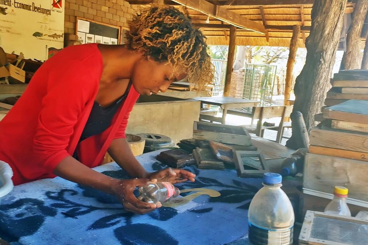 HEEED manager Violet Zacharia demonstrates how her team decorates recycled paper using crushed baobab flowers. Image by Charles Mpaka for Mongabay.