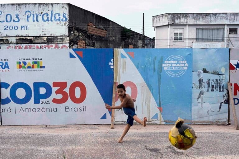 A boy kicks a soccer ball near signage for the COP30 U.N. Climate Conference in Belem, Brazil, March 23, 2025. Image by AP Photo/Jorge Saenz.