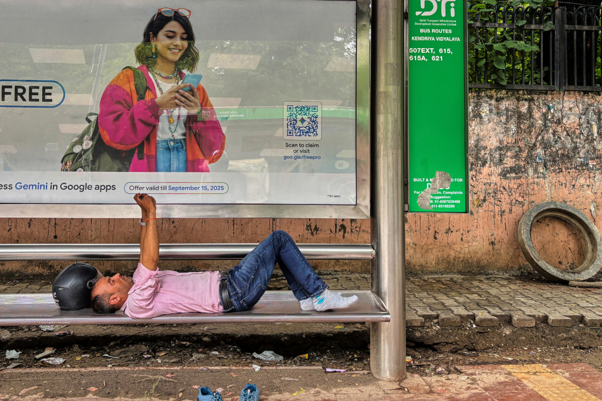 A commuter watches a video on his mobile phone lying down at a bus stop in New Delhi. Data indicate that more and more people get their news from social media and videos rather than traditional journalism outlets. Image by AP Photo/Manish Swarup.