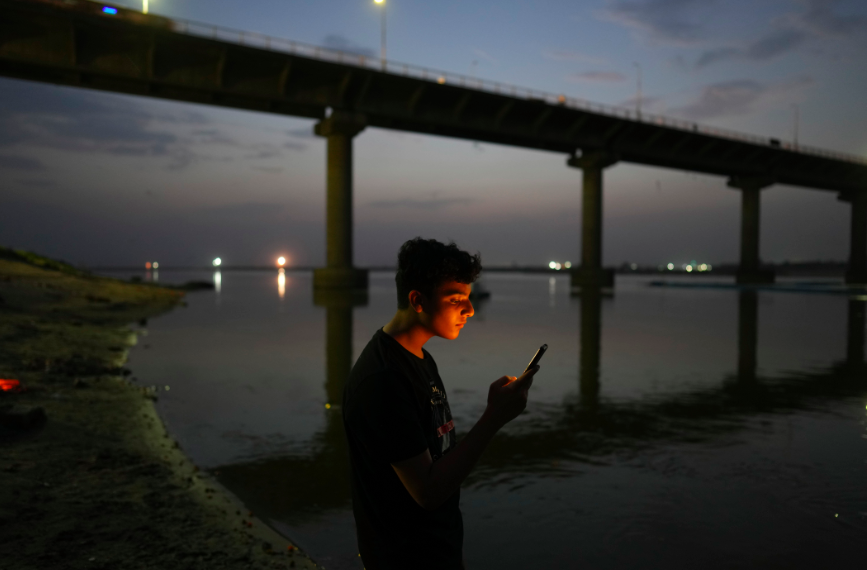 A youth checks his mobile phone on the bank of the River Ganges in Prayagraj, India. Recent research shows young people increasingly get their news on social media, video and online platforms. Image by AP Photo/Rajesh Kumar Singh, File.
