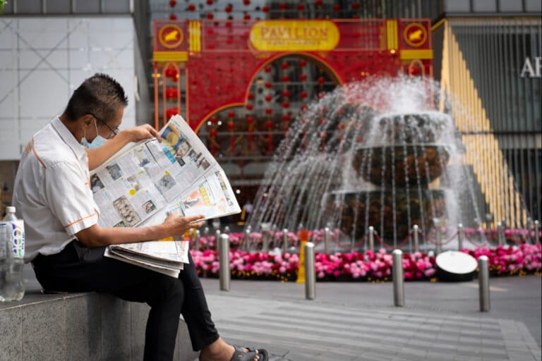 A man wearing a face mask reads newspaper outside a shopping mall in downtown Kuala Lumpur, Malaysia, in January 2021. Malaysian authorities imposed tighter restrictions on movement to try to halt the spread of COVID-19. Image by AP Photo/Vincent Thian.