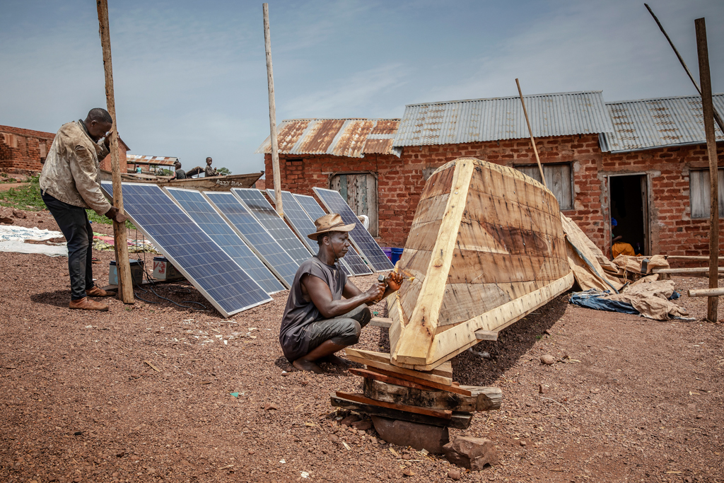 Solar panels charge batteries as a man fixes a traditional fishing boat near Lake Tanganyika in Kigoma, Tanzania. Image © FAO/Luis Tato.