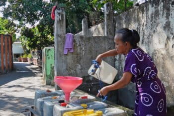 A woman in her 60s fills empty jerrycans in a wheelbarrow with water she draws from an old well in Tallo village, Makassar.