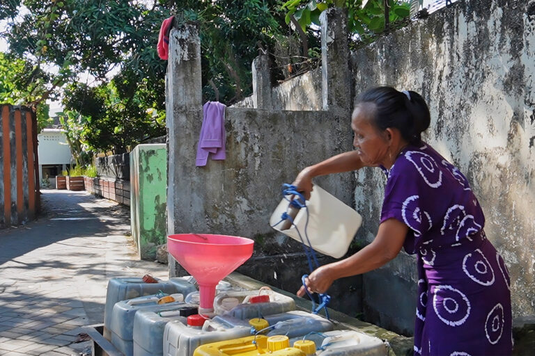 A woman in her 60s fills empty jerrycans in a wheelbarrow with water she draws from an old well in Tallo village, Makassar.