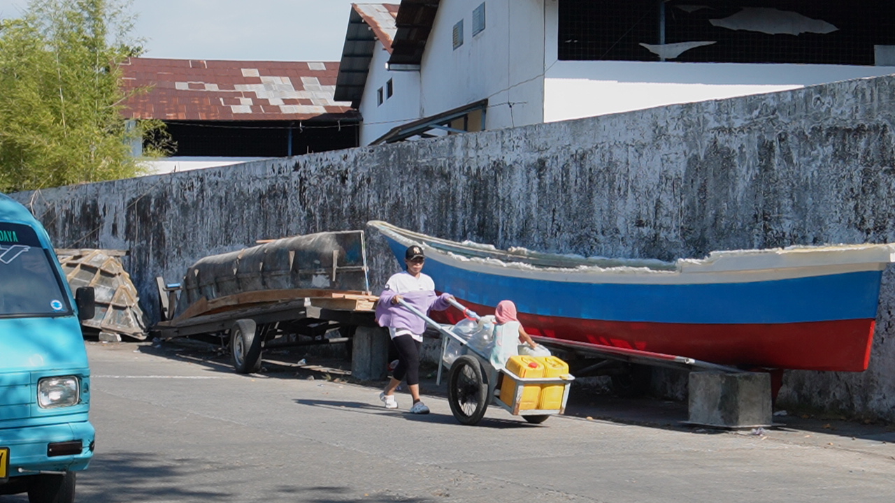 A woman on the coast of Makassar pushes a cart carrying clean water.