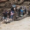 Flood survivors use logs to cross a river in Batang Toru, North Sumatra, Indonesia, on Dec. 2, 2025. Image by AP Photo/Binsar Bakkara.