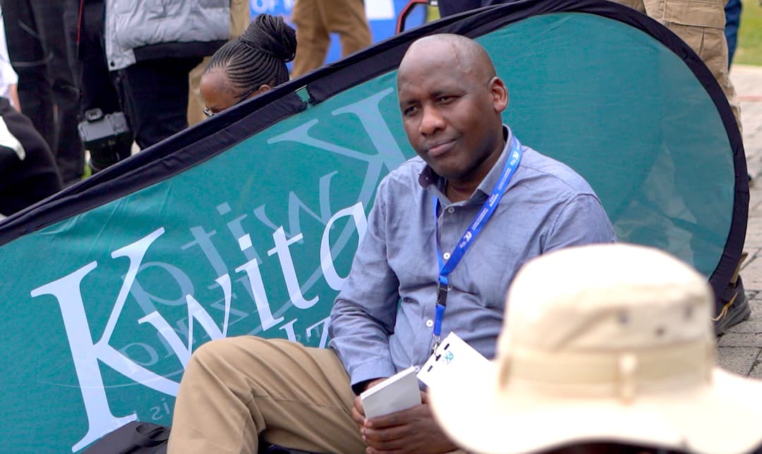 Twahirwa sits next to a sign of Kwita Izina, Rwanda’s flagship Gorilla Naming Ceremony, at the foothills of Volcanoes National Park in the village of Kinigi in northern Rwanda. Image courtesy of Jean Leonald Karuranga.