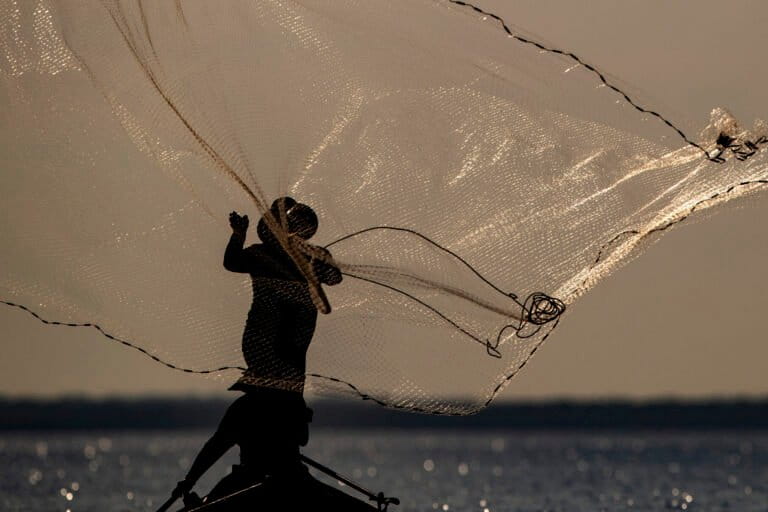 A fisherman is silhouetted as he casts his net into the Tapajos River in Santarem, Para state, 2020.