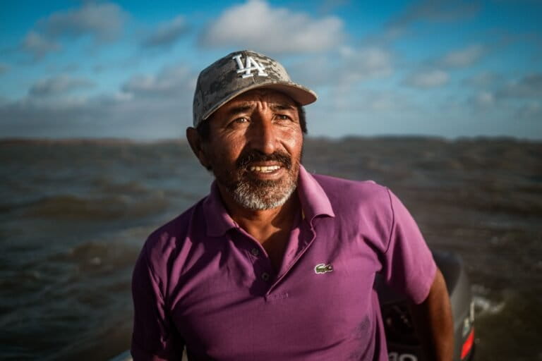 Wilfrido Arends, 46, an Indigenous Wayuu fisher known locally as “Caracas,” scans the horizon as he steers the onboard motor of his small fishing boat. Image by Euan Wallace.
