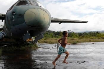 A Yanomami Indigenous child plays among the wreckage of a Brazilian Air Force aircraft at the Surucucu airport. Image courtesy of Fernando Frazão/Agência Brasil.