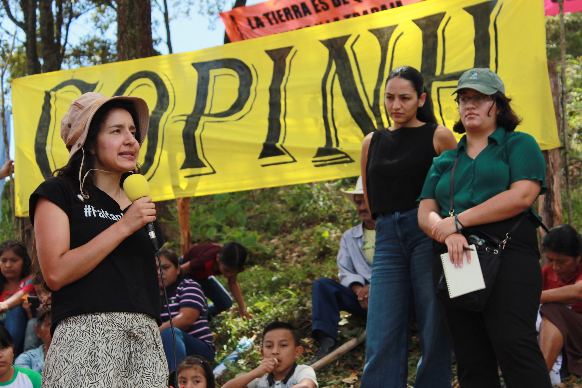 Bertha Zúñiga hablando con micrófono y lona detrás