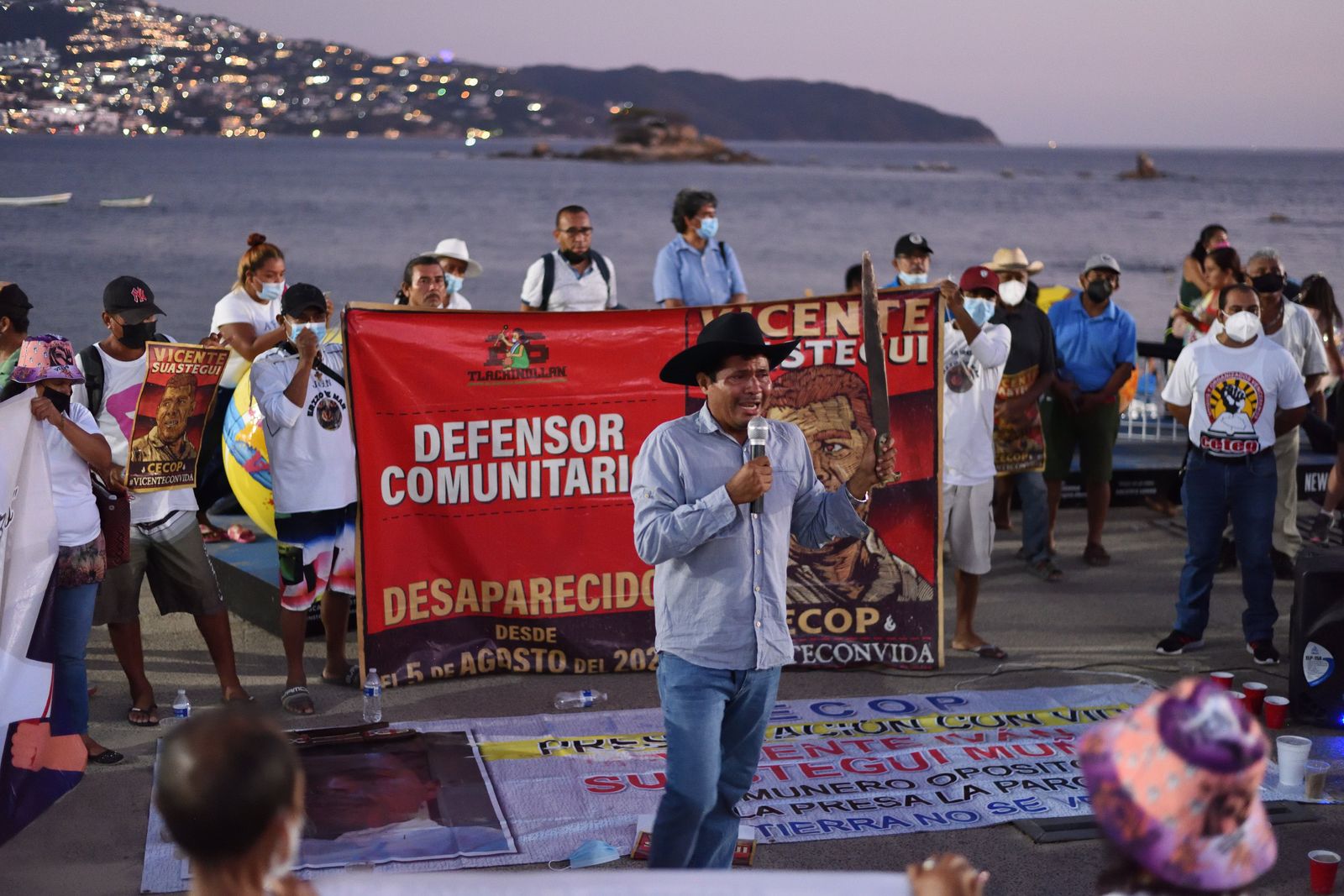 Hombre sujeta un machete con una pancarta de protesta de fondo