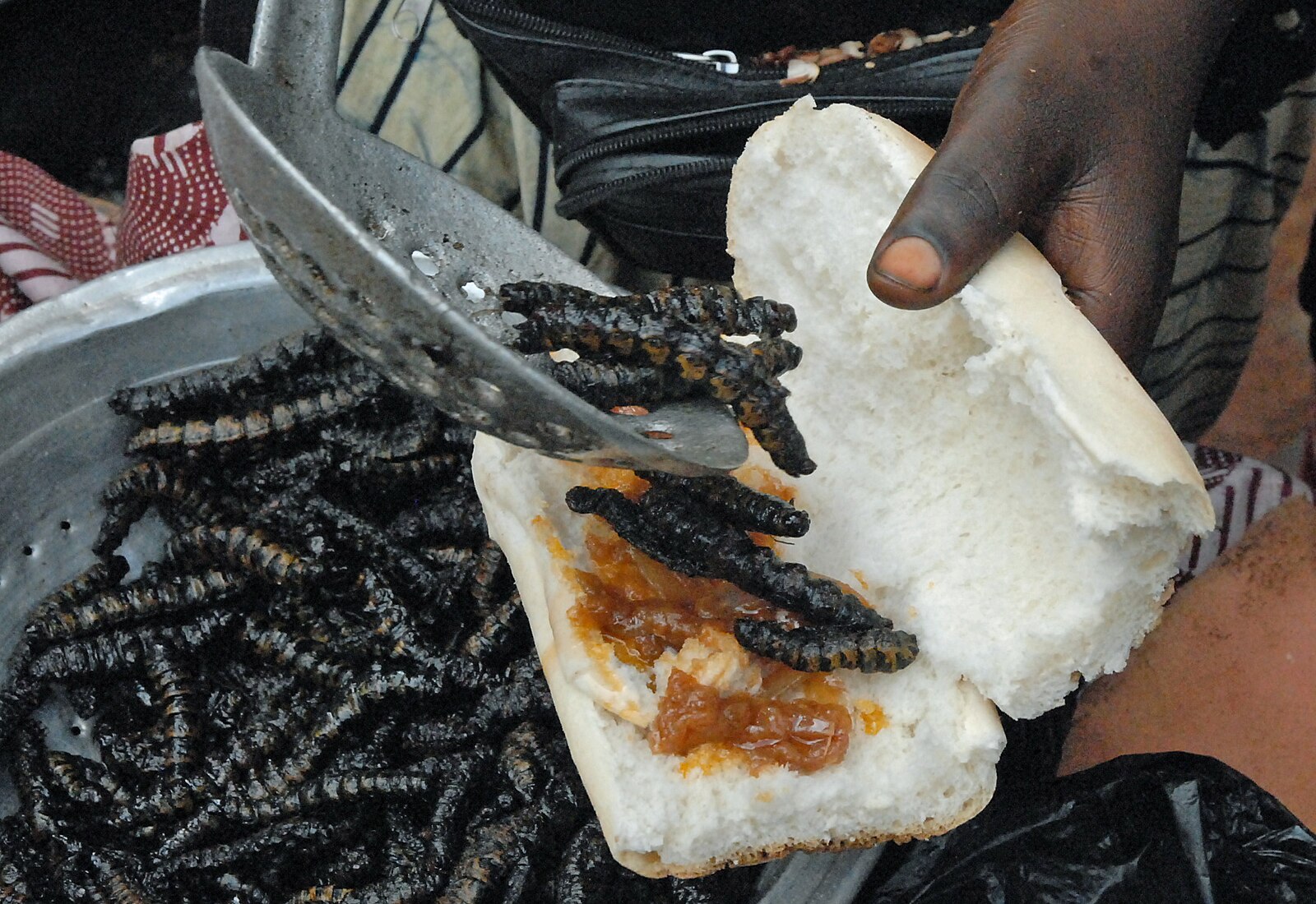 Préparer un sandwich avec des chenilles de karité frites à la gare routière de Boromo au Burkina Faso. Image de Rik Schuiling / TropCrop-TCS via Wikimédia Commons (CC BY-SA 4.0).