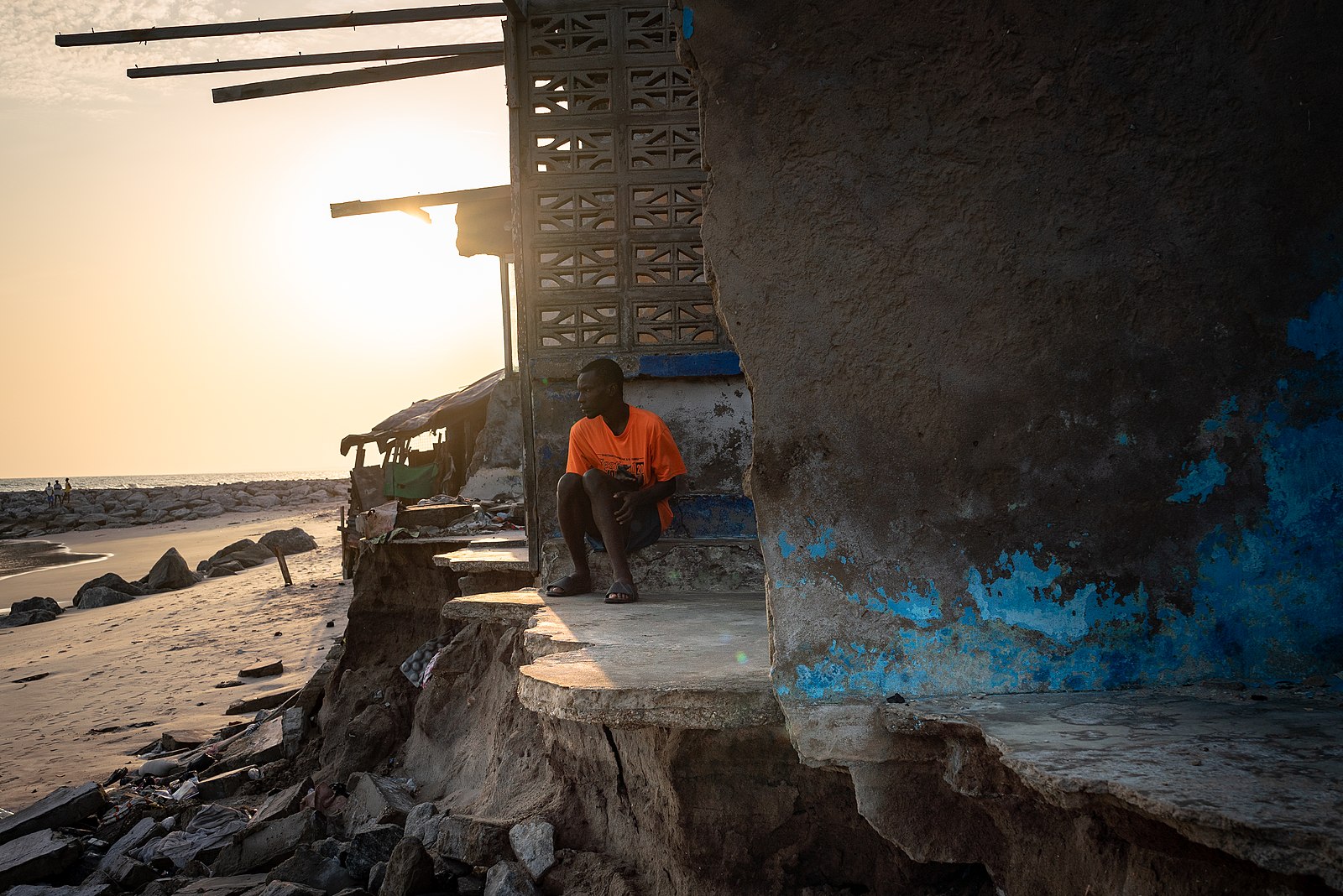 Un homme est assis devant une maison délabrée à Chorkor, une banlieue d'Accra, témoignant des effets de l'érosion côtière. La fonte des calottes glaciaires et la dilatation des océans due au réchauffement climatique entraînent une poussée de la mer vers le littoral ghanéen. Image de Ernest Ankomah Frimpong via Wikimédia Commons (CC BY-SA 4.0).