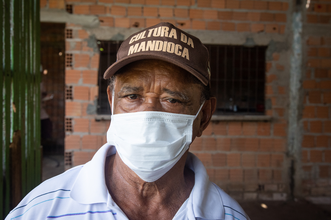 A photo of Seu Catirinha wearing a medical mask and a baseball cap that says "Cassava Culture."