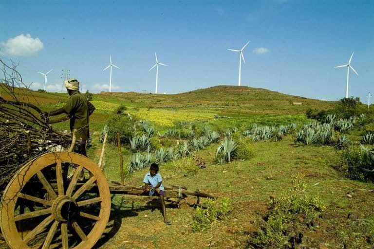 A person collecting fossil fuel in front of wind turbines. The United Nations estimates that the entire world has to achieve net-zero emission by 2050 to stay under 2-degree Celsius warning at the pre-industrial level and India is under tremendous pressure to announce its own net-zero year. Photo- Vestas/Yahoo/Wikimedia Commons