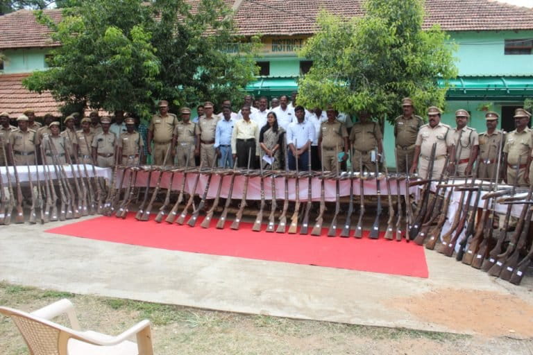 Image shows a group of government officials posing with a cache of seized guns