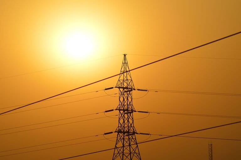 Image shows an electricity transmission tower with the Sun in the background