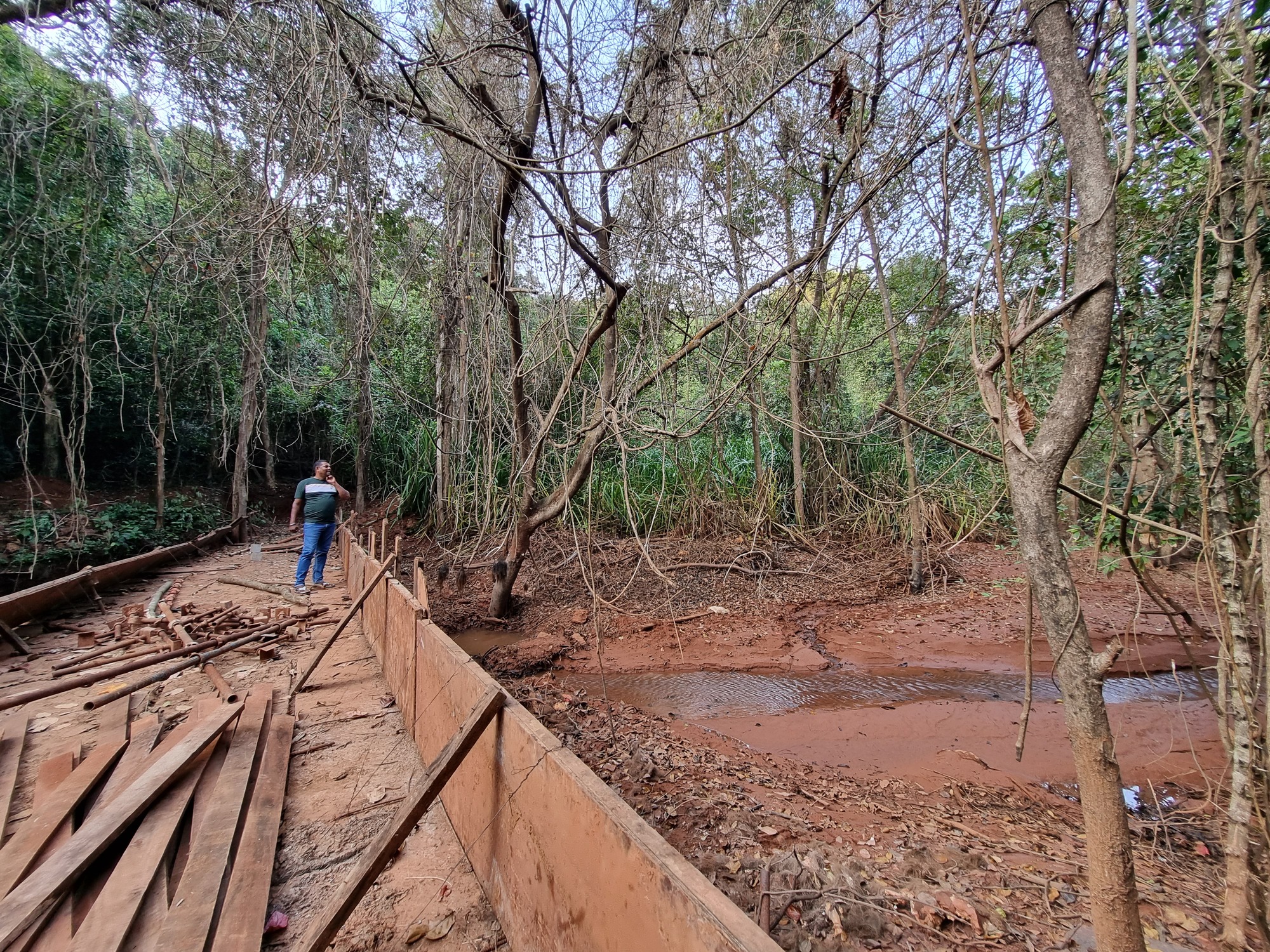 Image shows a man standing on a bridge with a small stream flowing by