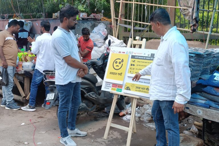 Aslam Khan, a street vendor in Delhi, explains the information displayed on a heat alert board to a tourist next to his garment cart. These colour-coded boards were launched by the India Meteorological Department as part of a unique collaboration with informal worker organisations and Greenpeace to improve weather warning systems. Image by Anuja.